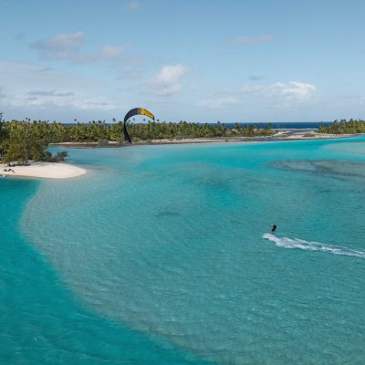 Kitesurfer on turquoise water near green island under a blue sky.