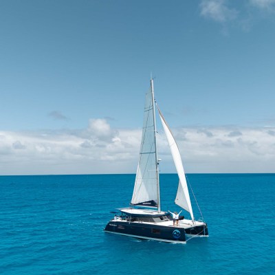 Sailboat with white sails on a clear blue sea under a slightly cloudy sky.
