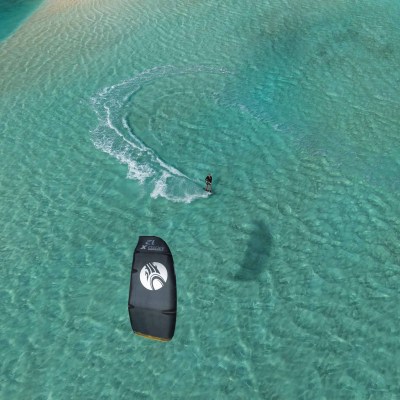 Aerial view of kite surfer on turquoise water near sandy beach.
