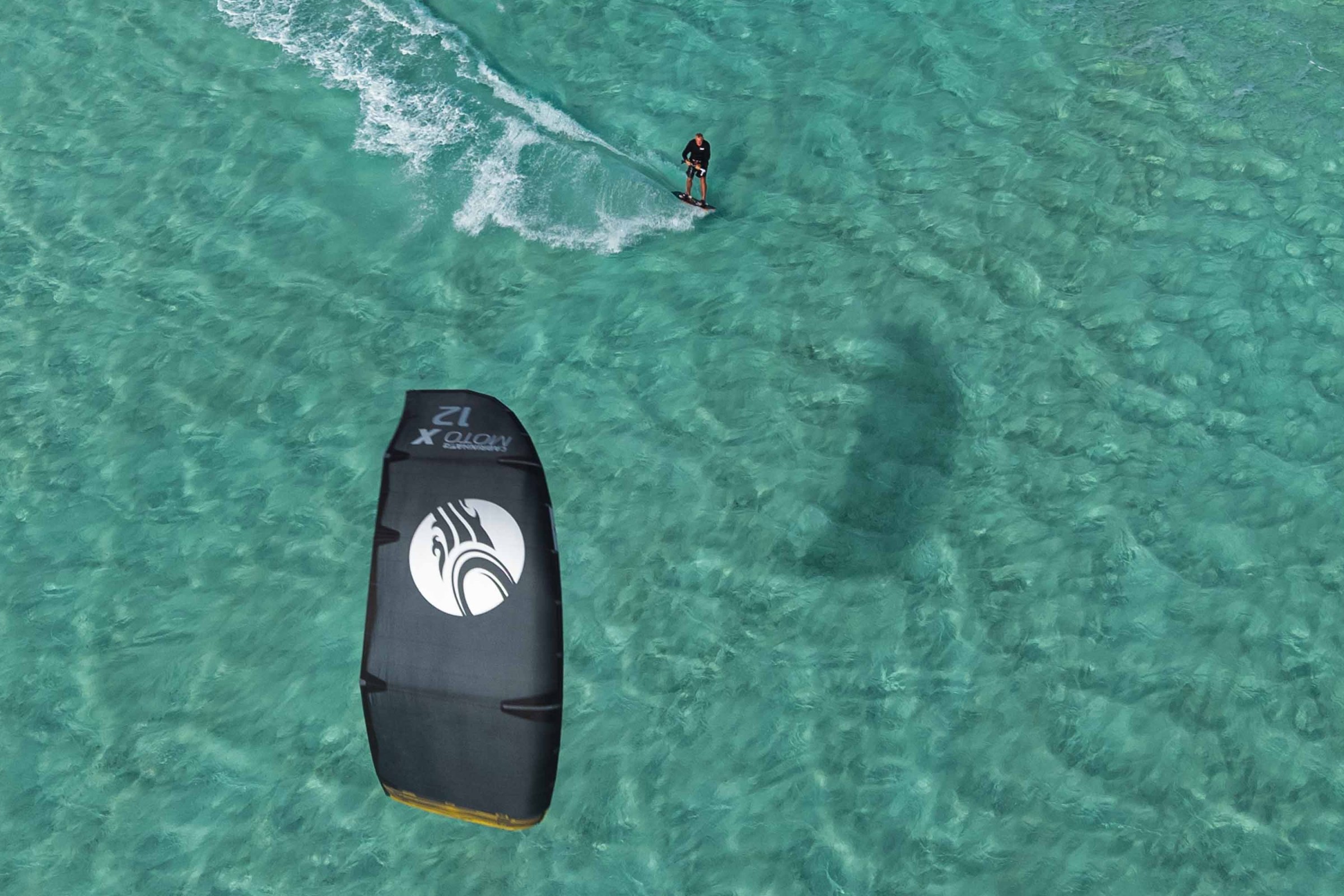 Aerial view of a person kiteboarding on clear turquoise water.