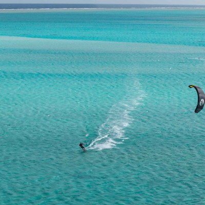 Person kitesurfing on turquoise ocean with clear skies.