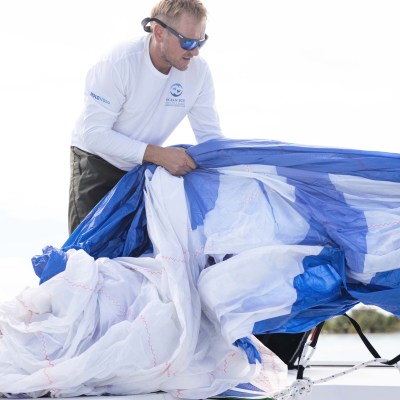 Person on boat handling blue and white sail with sunny sky.