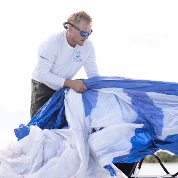 Person handling a large blue and white sail outdoors.