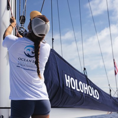 Person adjusts sails on a boat named HOLOHOLO on a sunny day.