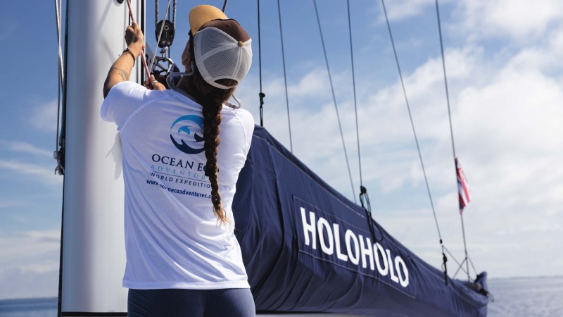 Person adjusts sails on a boat named HOLOHOLO on a sunny day.