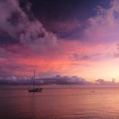 Sailboat on calm sea beneath vibrant pink and purple sunset clouds.