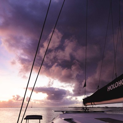 Sailboat at sunset with a cloudy sky and mast labeled 'HOLOHOLO'.