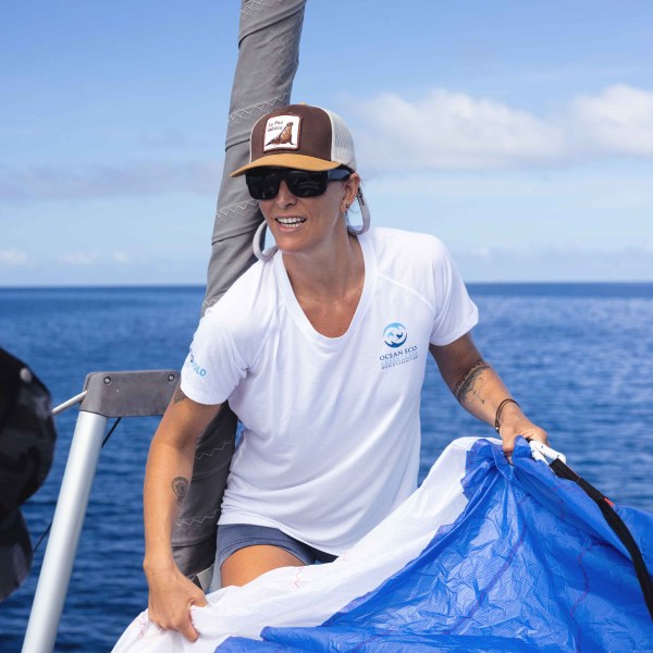 Person in white shirt on a boat holding a blue sail.