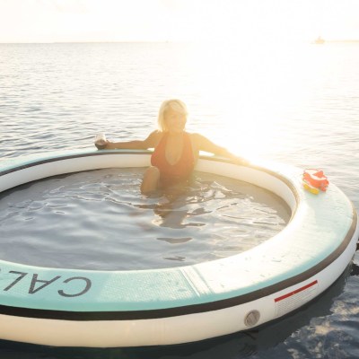 Person in a circular floatation device on calm water at sunset.