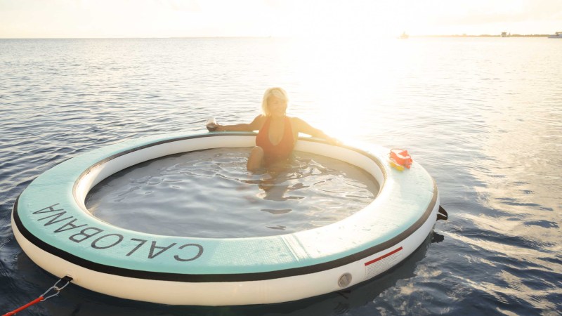 Person in red swimsuit sits on large round float in the sea.