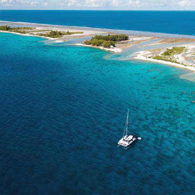 Aerial view of a sailboat in clear blue ocean near a scenic island.