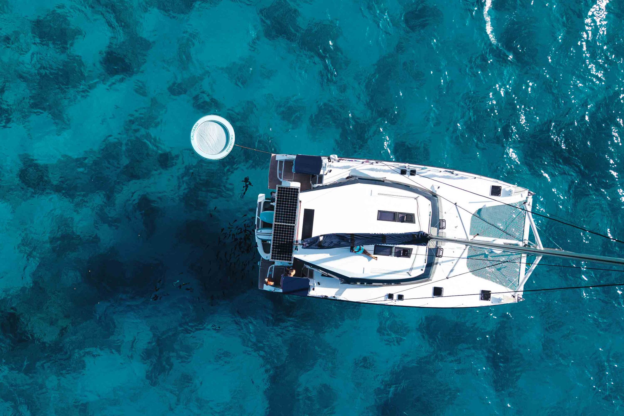 Aerial view of a white sailboat on clear blue water.