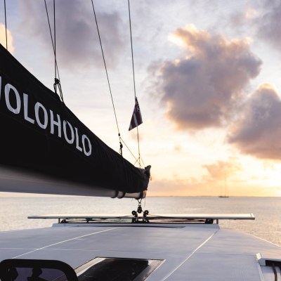 Sailboat at sunset with 'HOLOHOLO' on sail, calm sea view.