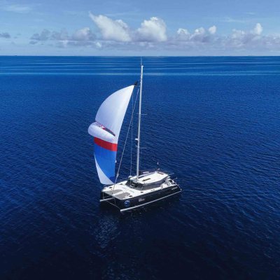 Sailboat with colorful sail on calm blue ocean, under a clear sky.