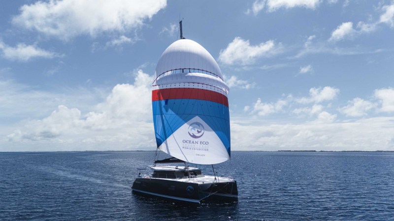 Sailboat with large colorful sail on the open sea under a blue sky.