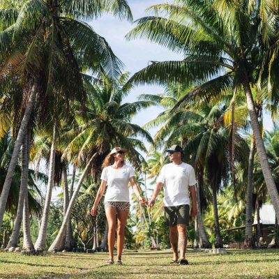 Couple walking hand in hand under tall palm trees on a sunny day.